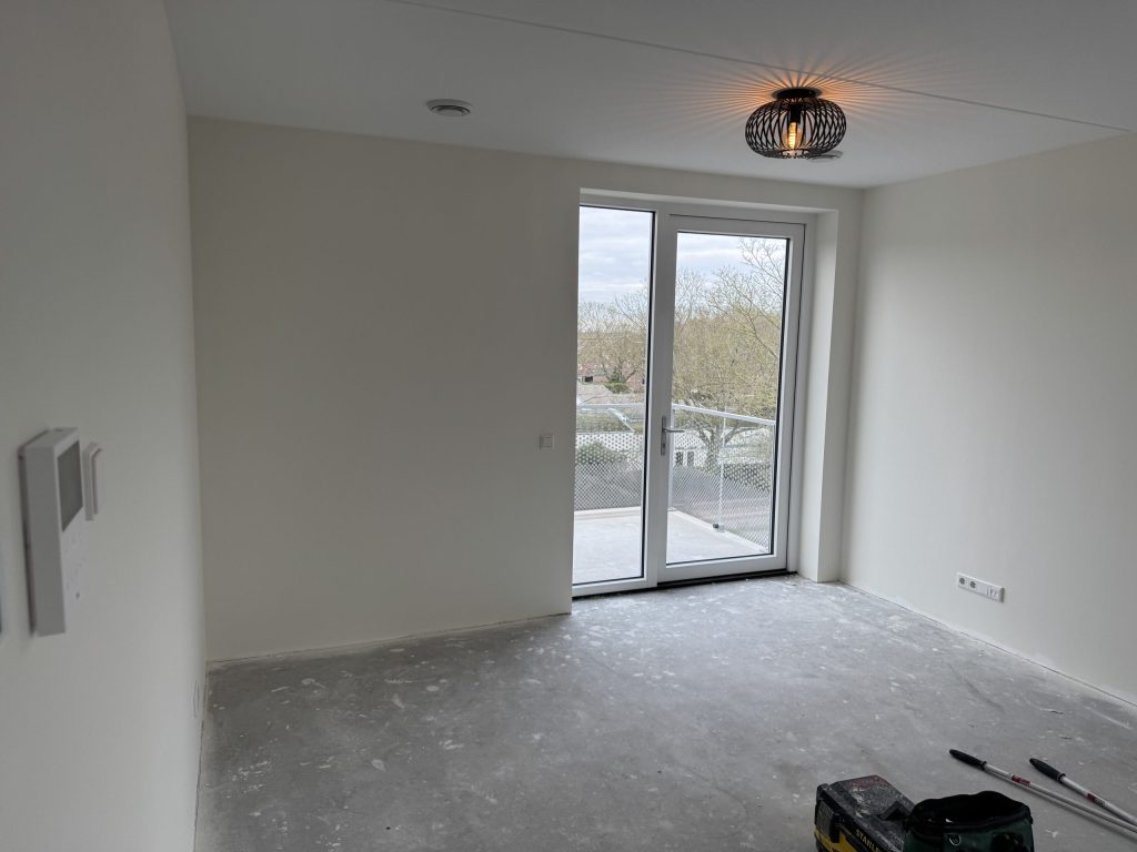 Lege kamer in een nieuw appartement met balkondeur en lichte wanden, kort na de oplevering