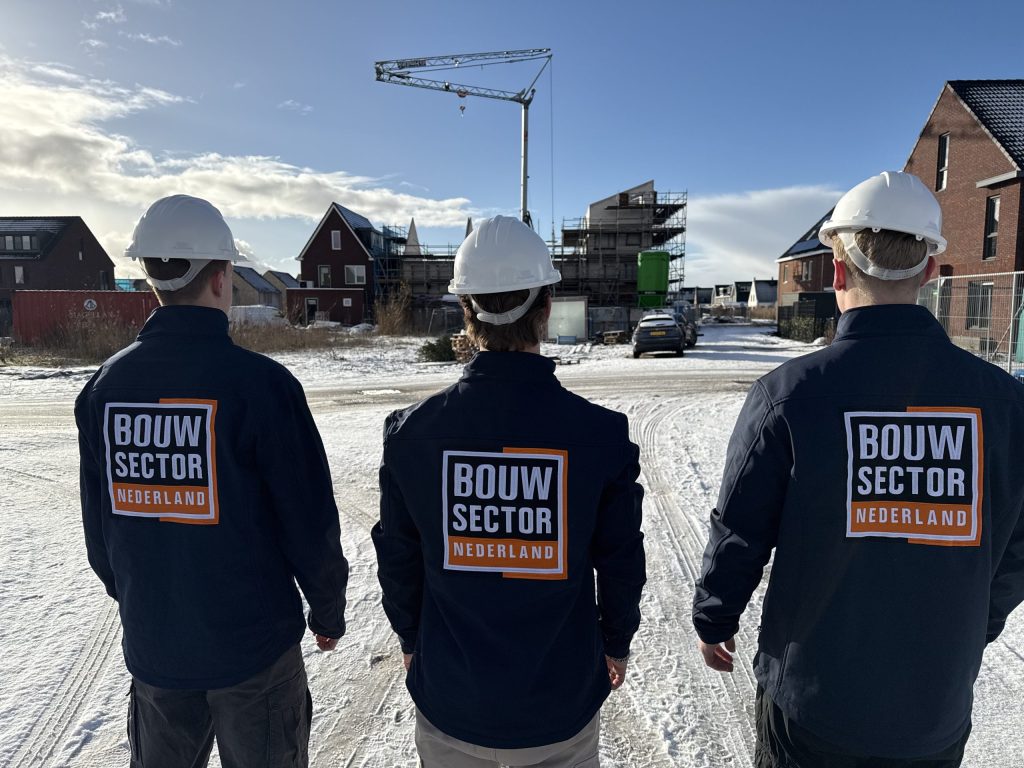 Drie vakmensen van Bouwsector Nederland met witte helm op een nieuwbouwlocatie met een bouwkraan